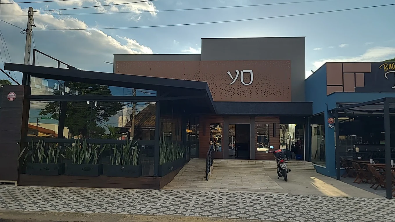 Modern building with a glass-walled patio and a brown sign that reads 'YO' above the entrance, next to a parked motorcycle.